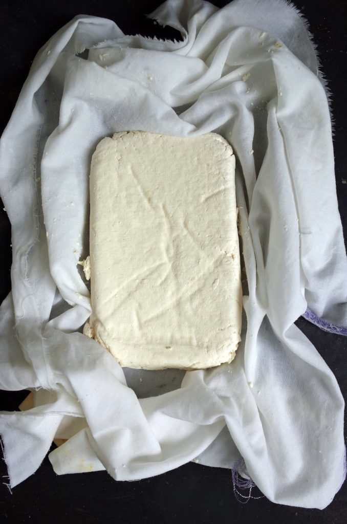 A block of homemade tofu made from soy milk on a cheesecloth