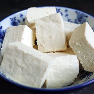 Homemade firm tofu made from soy milk cut into pieces and in a Chinese white and blue bowl