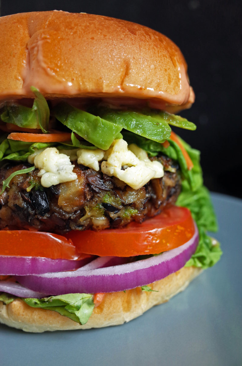 Close up photo of a vegetarian mushroom burger patty in a brioche bun with salad, cheese and avocado
