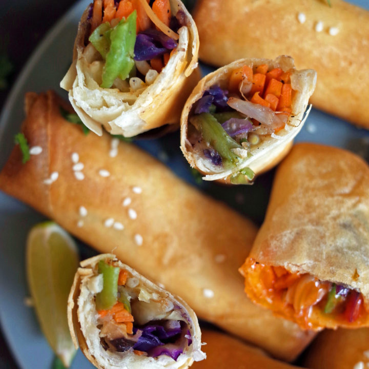 Crispy Vegetable Spring Rolls displayed with sesame seeds, lime and coriander on a blue plate