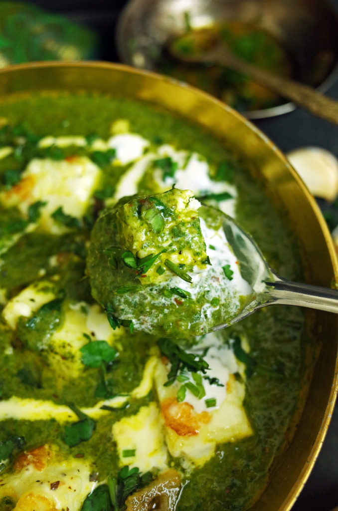 Palak Paneer topped with cream and coriander being scooped by a metal spoon