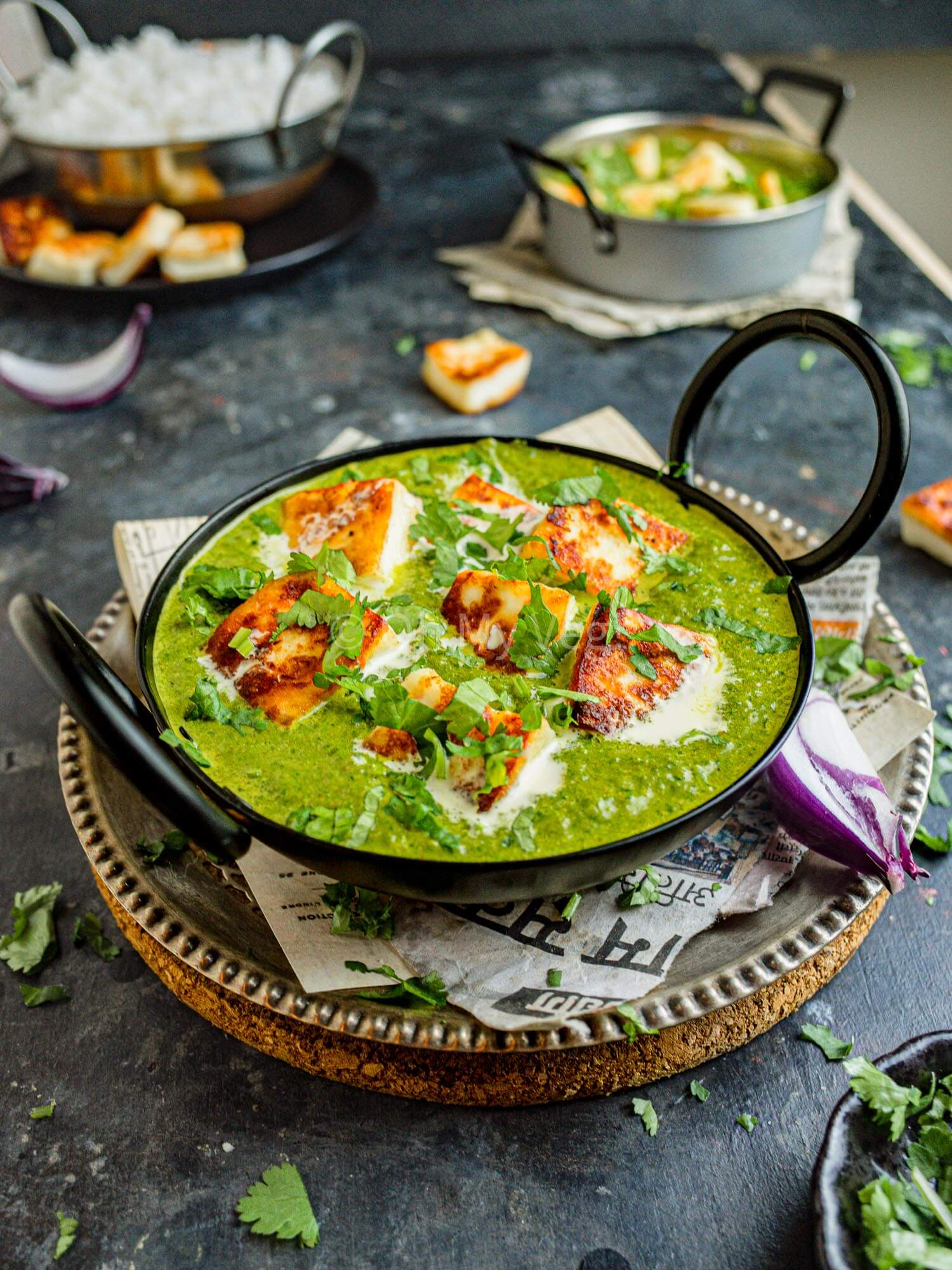 Palak paneer in a black kadai, with onion on the side, on a black background.