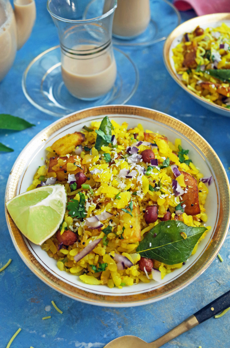 Kanda Batata Poha in a white and gold bowl with Lemon and Chai on a blue background