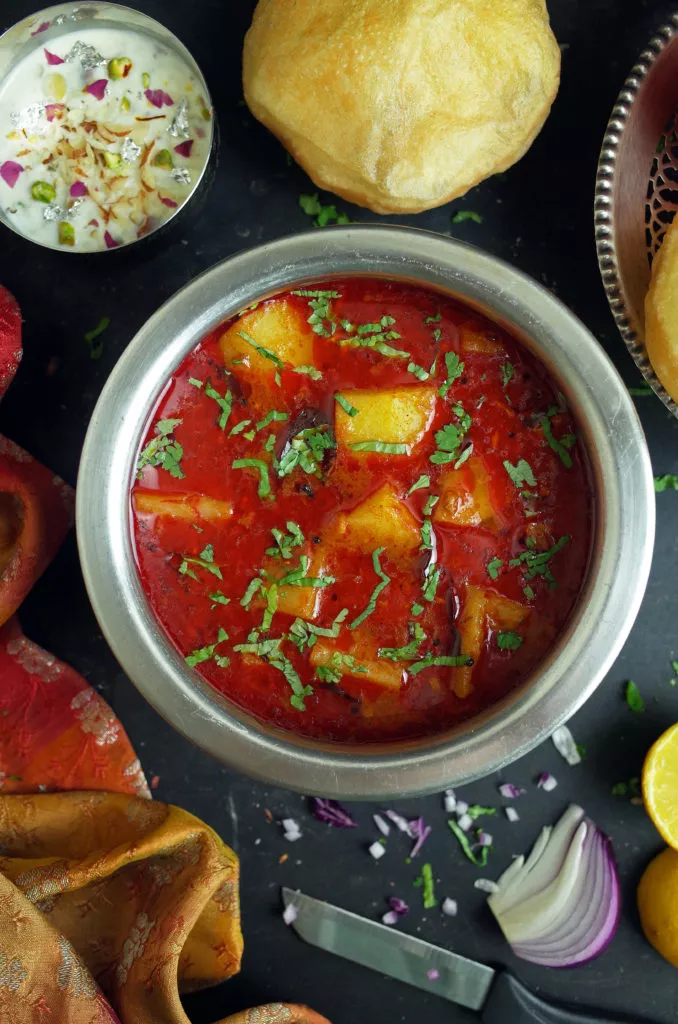 Maharashtrian Batata Rassa Potato Curry in a steel bowl with Puri and Kheer