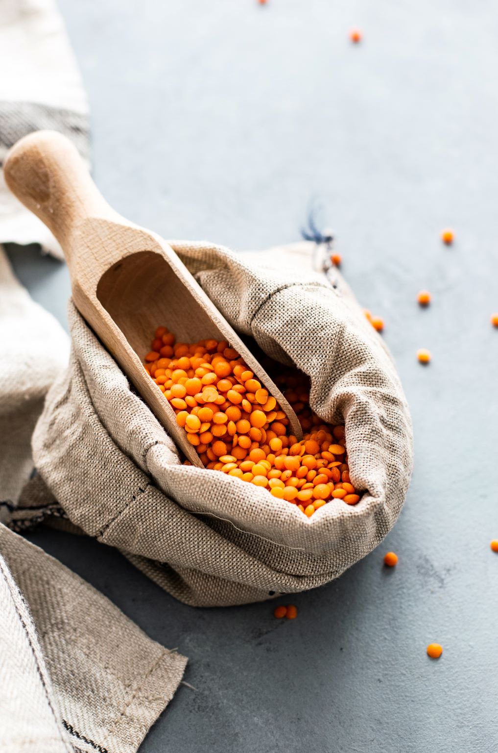 A wooden scoop taking red lentils from a cloth bag