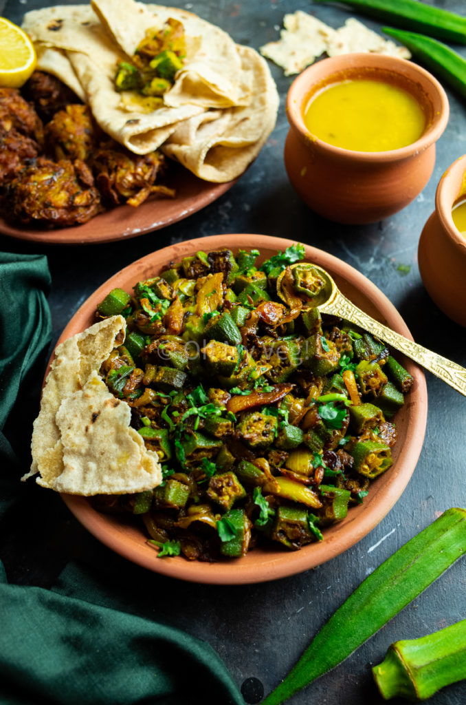 Bhindi Masala in a clay bowl, with torn chapati roti and Dal, Onion Bhaji in the background