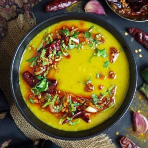 A black bowl full of yellow Indian Dal Tadka topped with a spicy tempering