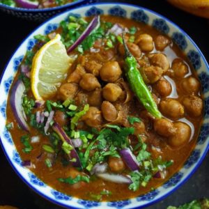 Vegan Chana Masala, Indian Chickpea Curry topped with green chilli and lemon in a blue bowl