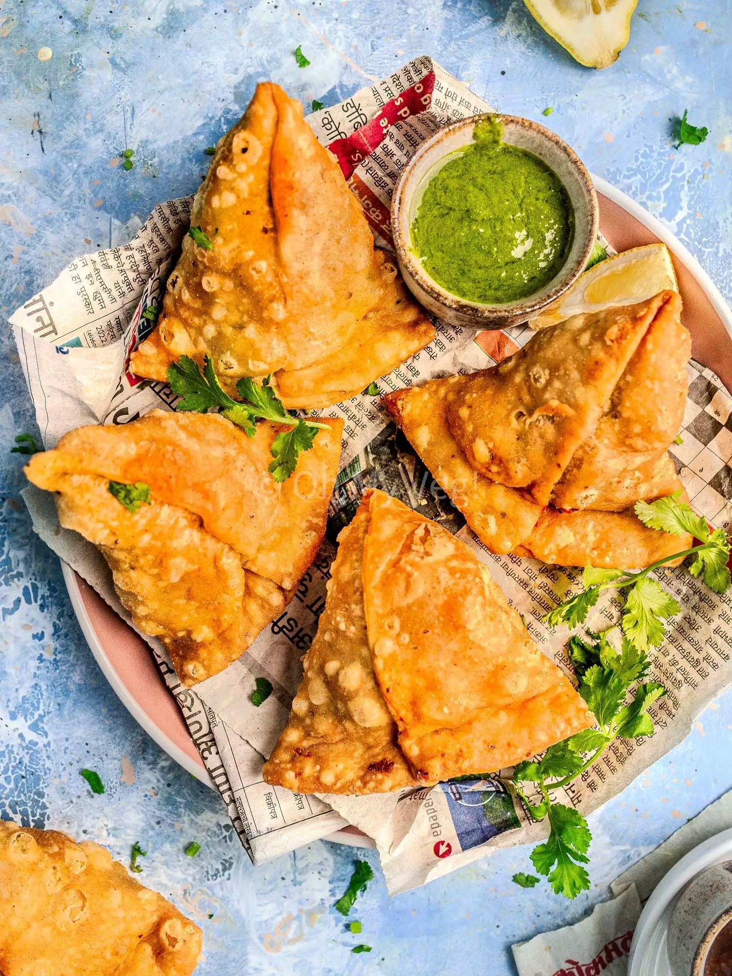 Punjabi vegetable samosa on a plate with a pot of green chutney.