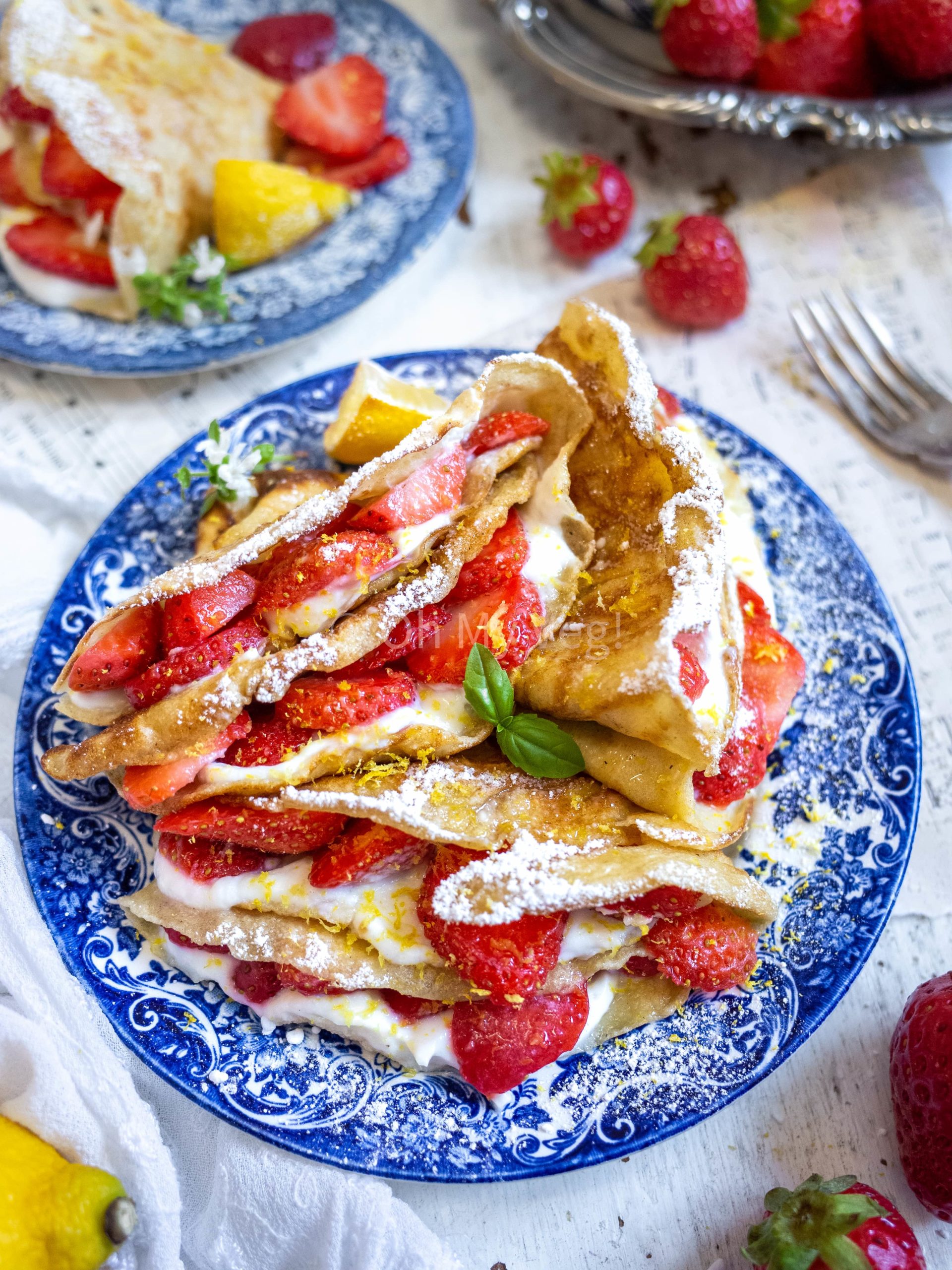 Folded crepes with whipped lemon ricotta cream and fresh strawberries on a blue plate