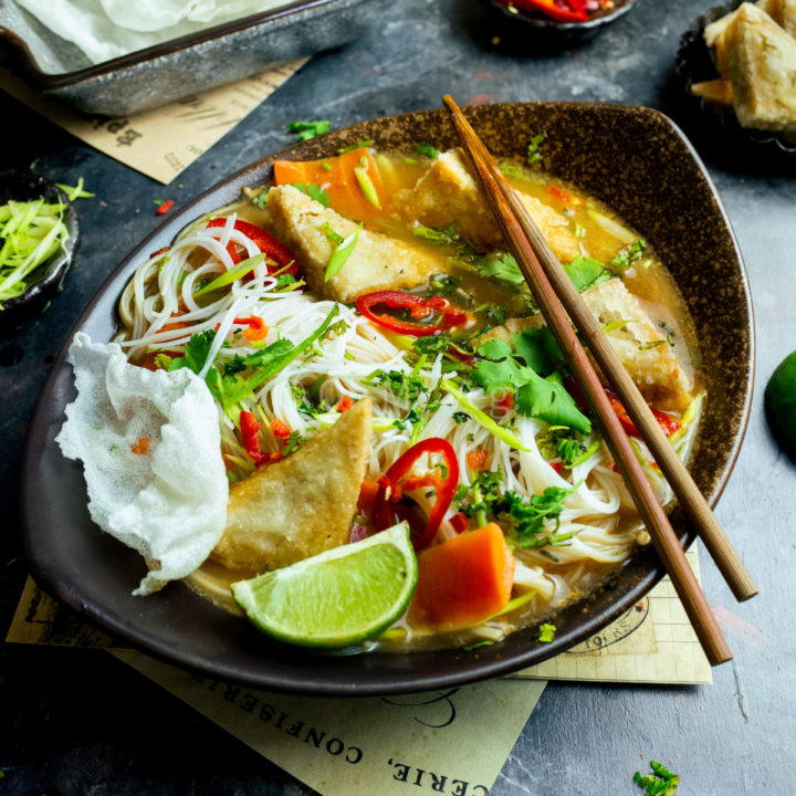 Chopsticks laying across a bowl of vegetarian tofu tum yum with vermicelli noodles