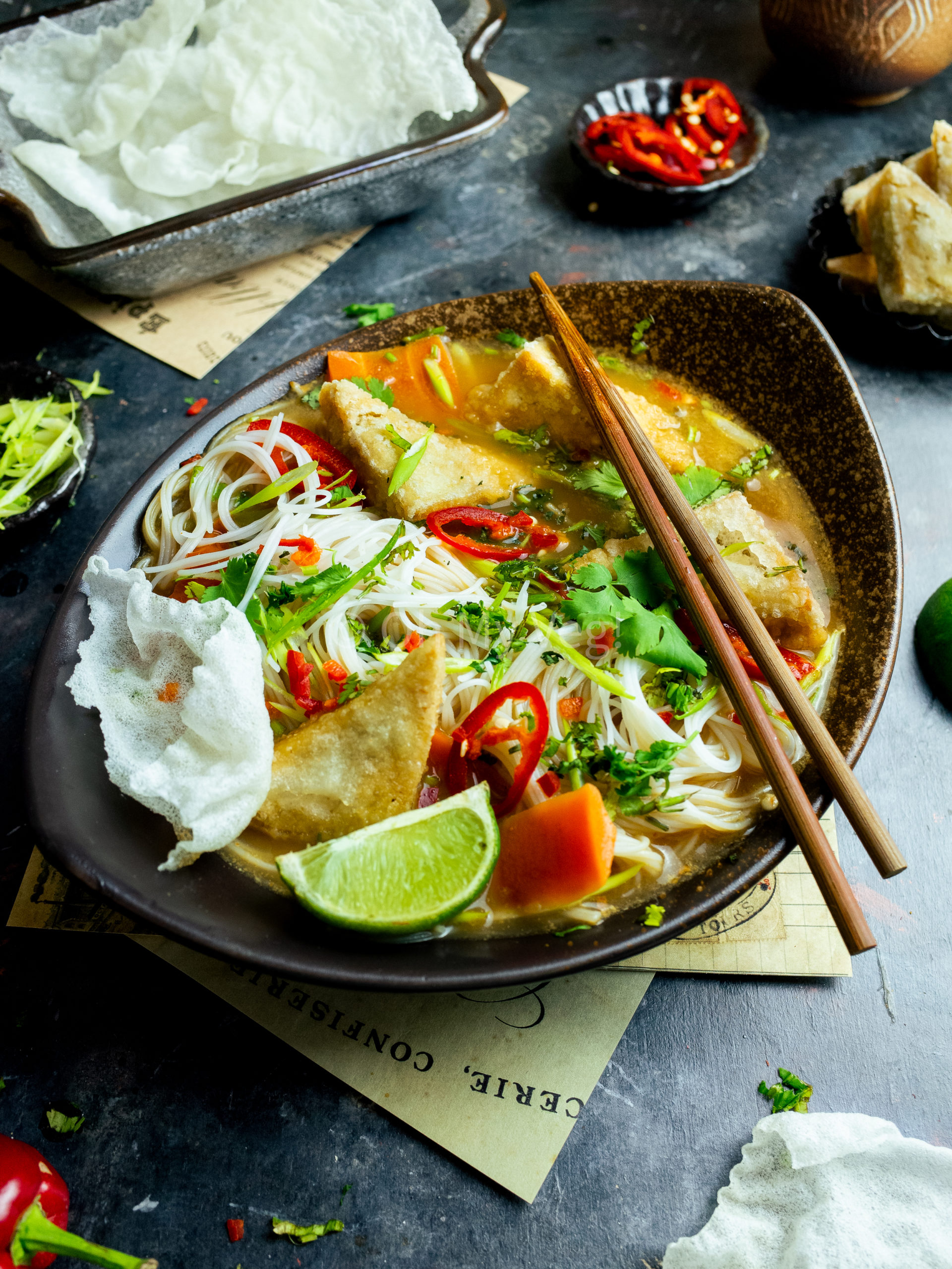 Chopsticks laying across a bowl of vegetarian tofu tum yum with vermicelli noodles