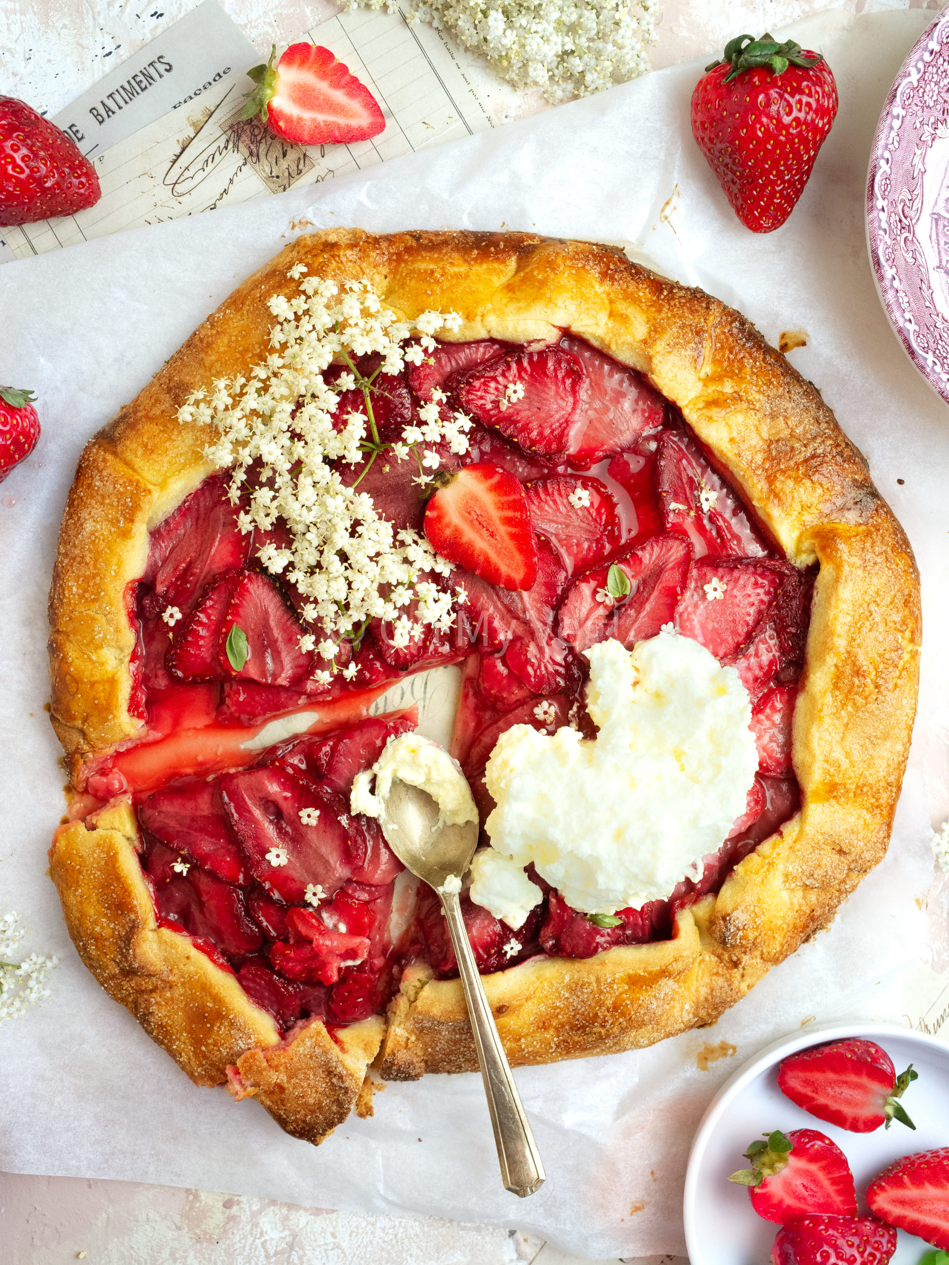 Strawberry and elderflower galette topped with whipped cream and a slice taken out