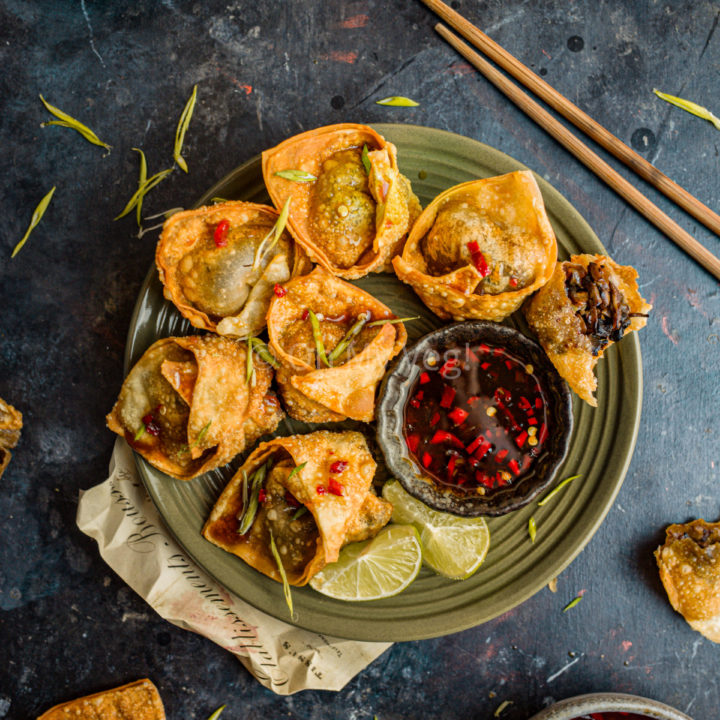 Fried vegan mushroom wontons on a plate with limes and sweet chili sauce