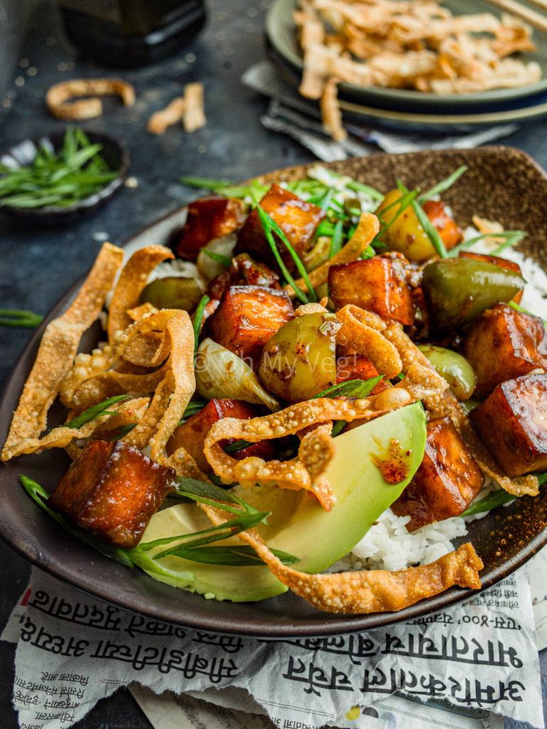 Chilli paneer in a bowl with avocado and wonton crisps, and garnished with spring onions.