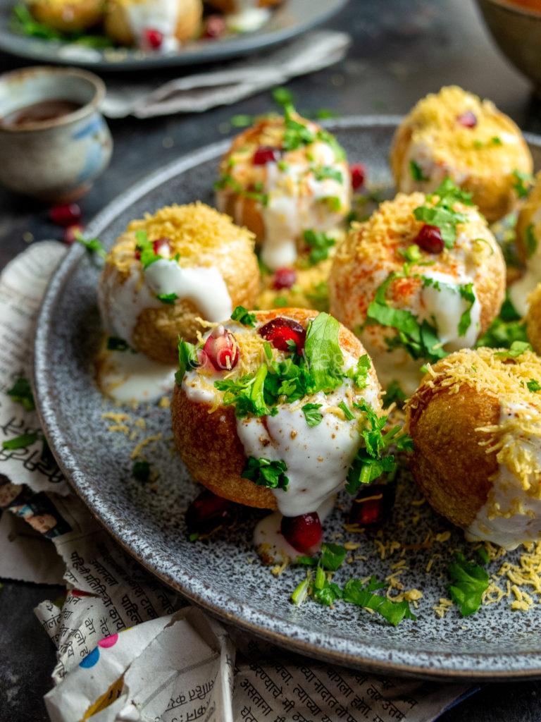 Close up photo of dahi puri chaat bombs on a grey plate with newspaper. 