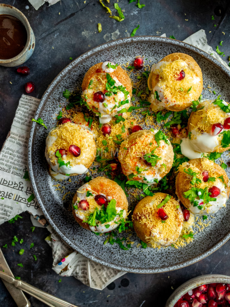 Dahi puri chaat bombs on a speckled grey plate with newspaper in the background. 