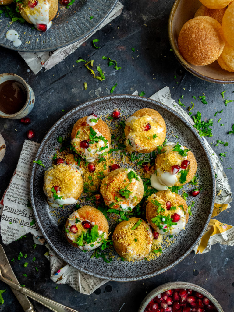 Dahi puri chaat bombs on a grey plate with newspaper in the background.
