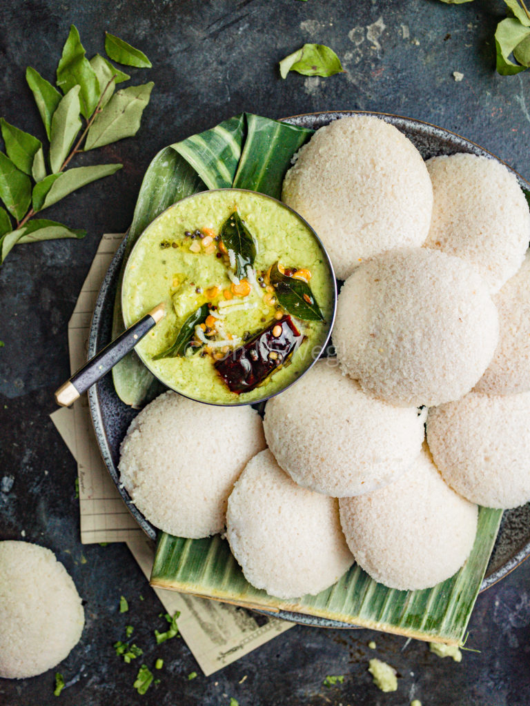 Fluffy idli on a plate with green coconut chutney. 