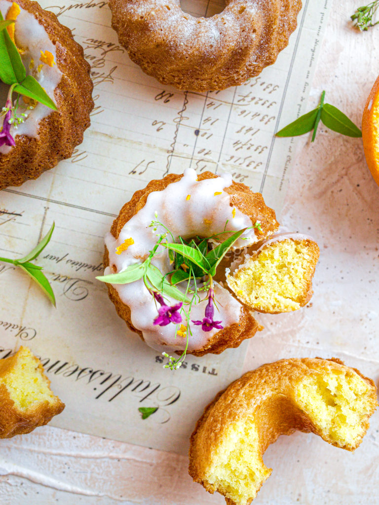 Orange and cardamom mini bundt cakes with an orange blossom glaze on vintage paper.