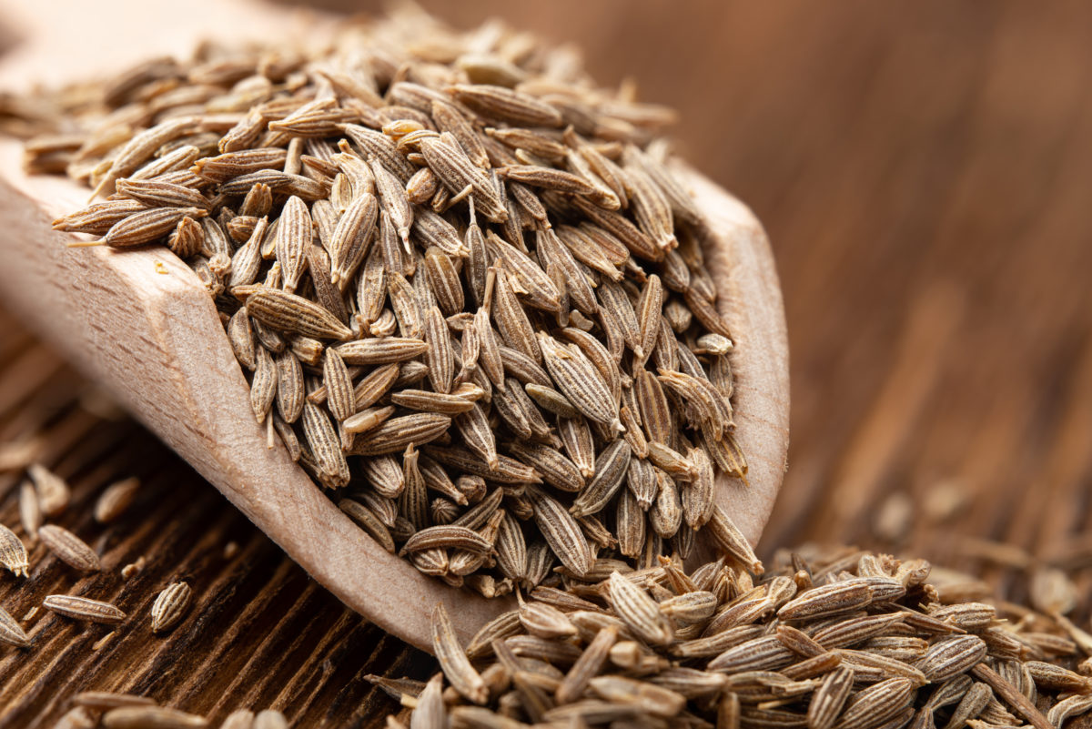 Close up of cumin seeds spilling out of a wooden spoon.