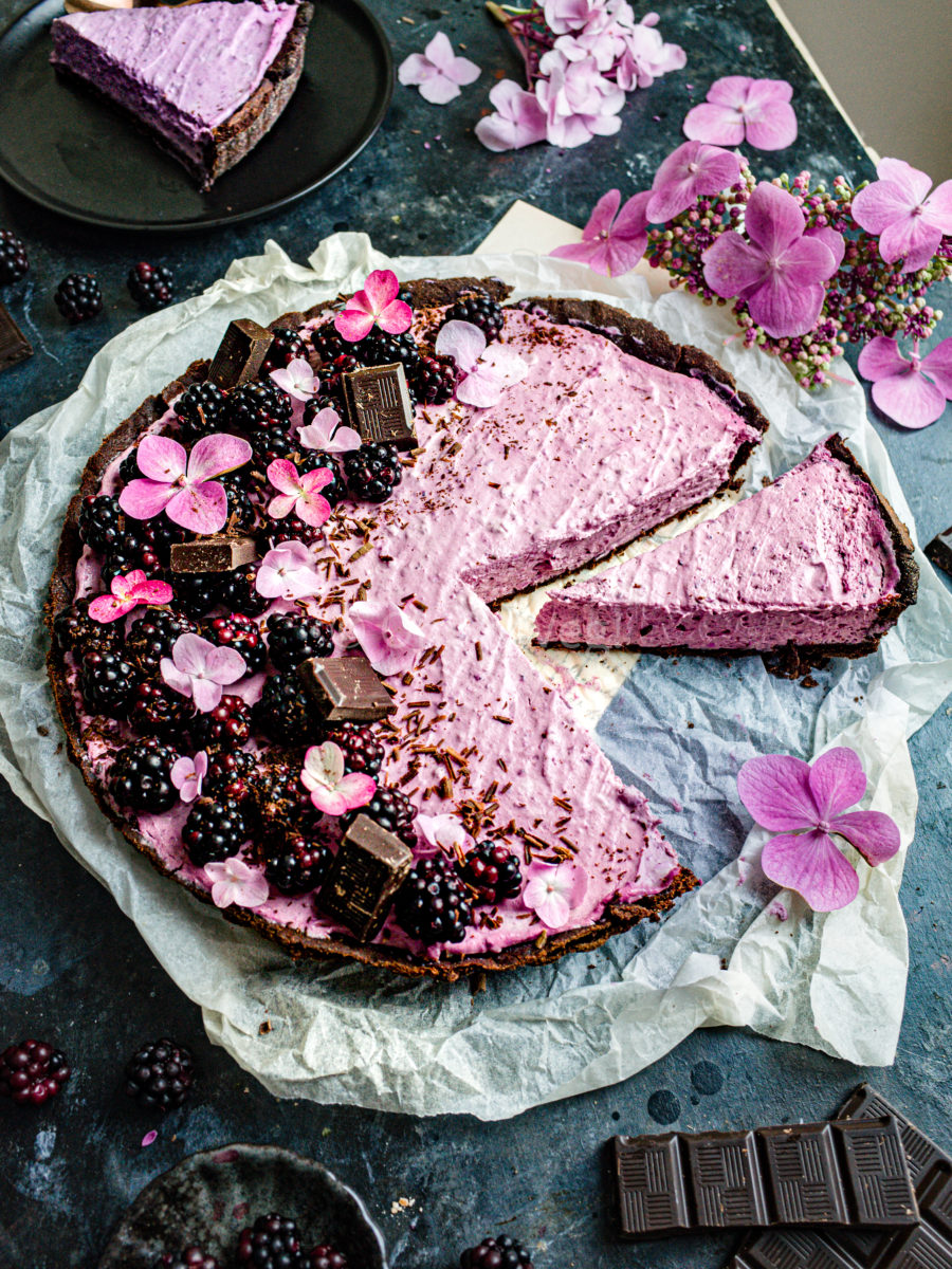 Blackberry tart decorated with chocolate, fresh blackberries, and hydrangea flowers with two slices cut out. 