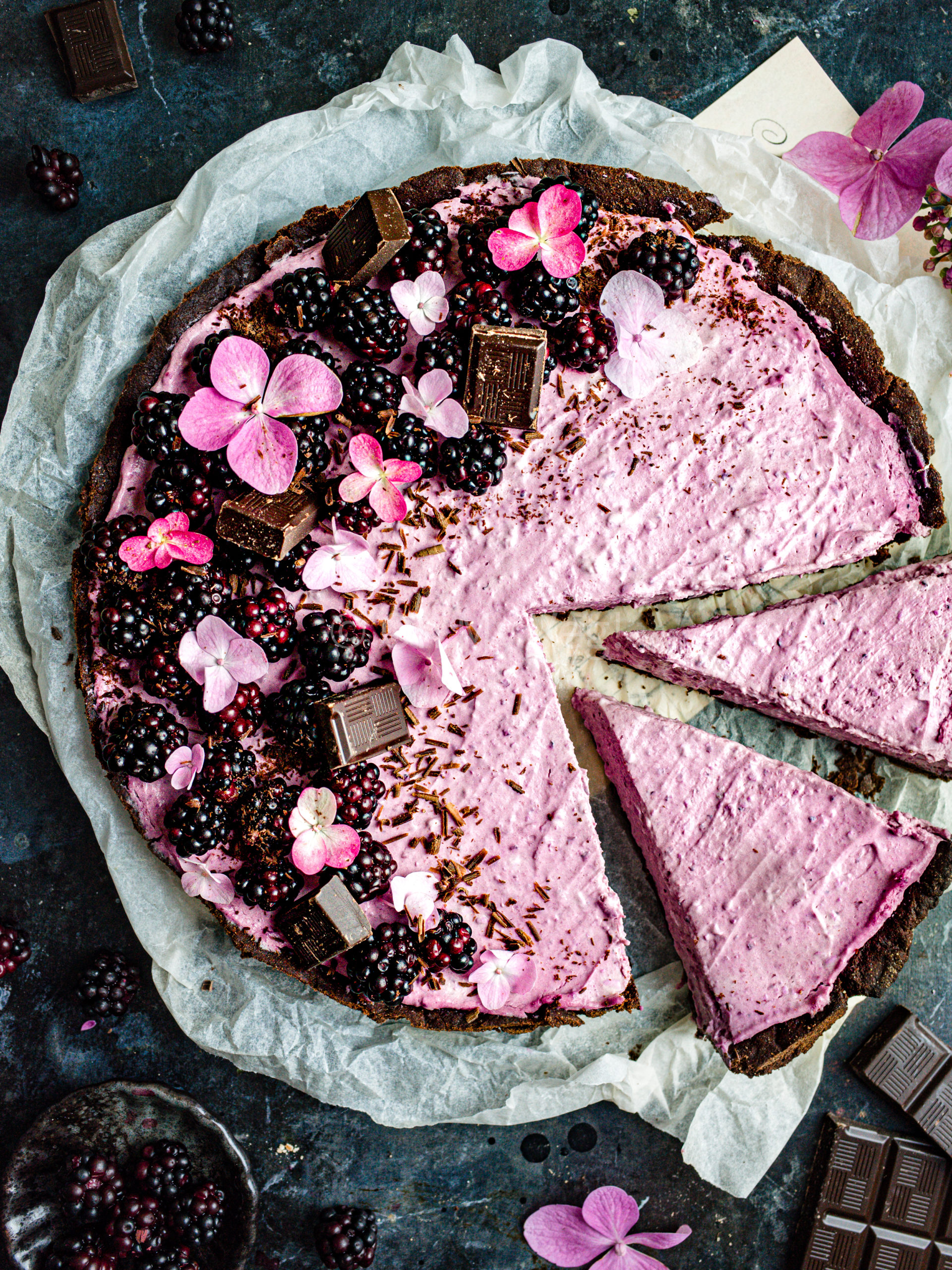 Blackberry tart with chocolate and flowers on a dark blue background. 