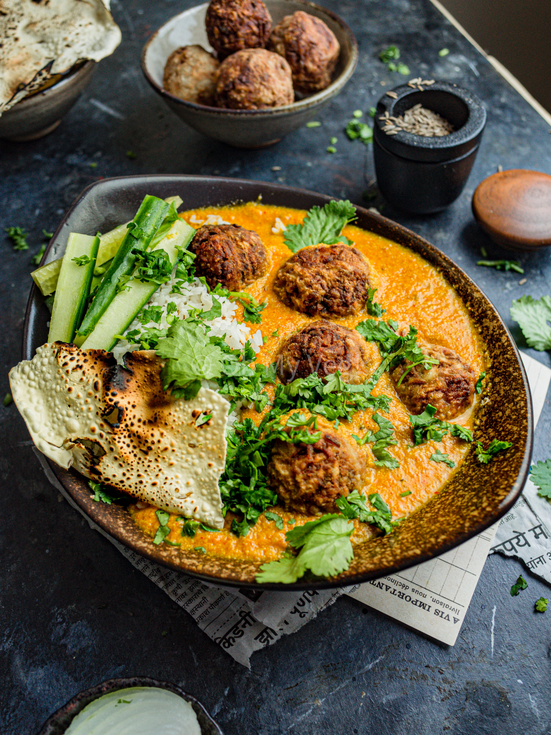 Lauki kofta with rice, cucumber, and papad in a brown bowl.