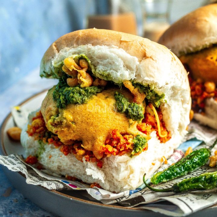 Vada pav on a blue background alongside fried green chilis.