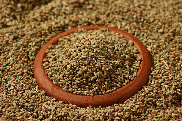 A small clay bowl full of carom seeds, with more carom seeds covering the whole background.