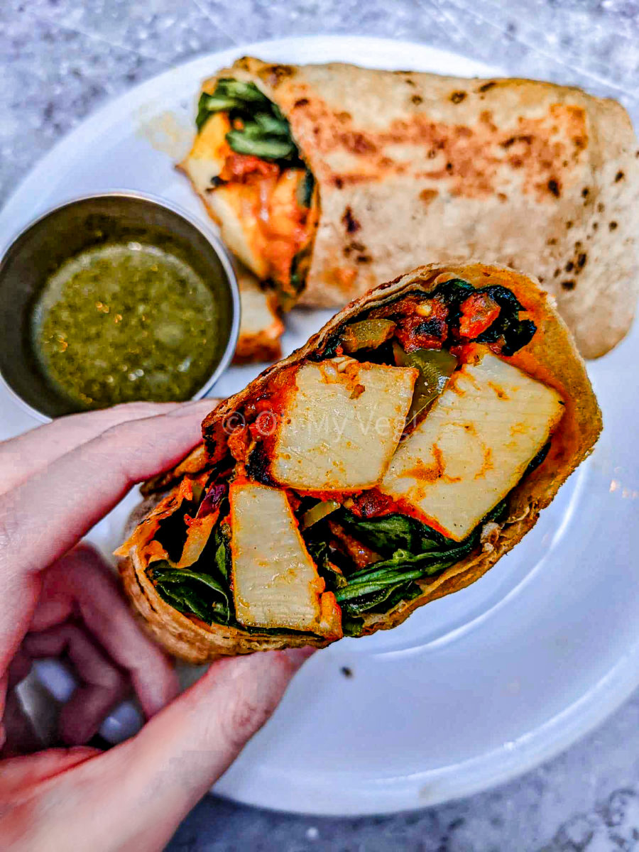 White hand holding one half of Dishoom's paneer roll with mint chutney. 
