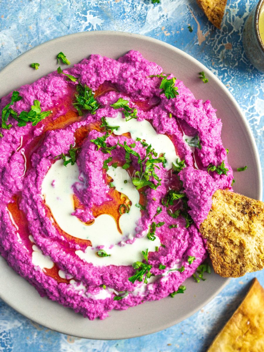 Beetroot hummus topped with oil and garlic tahini sauce, with pita chips. 