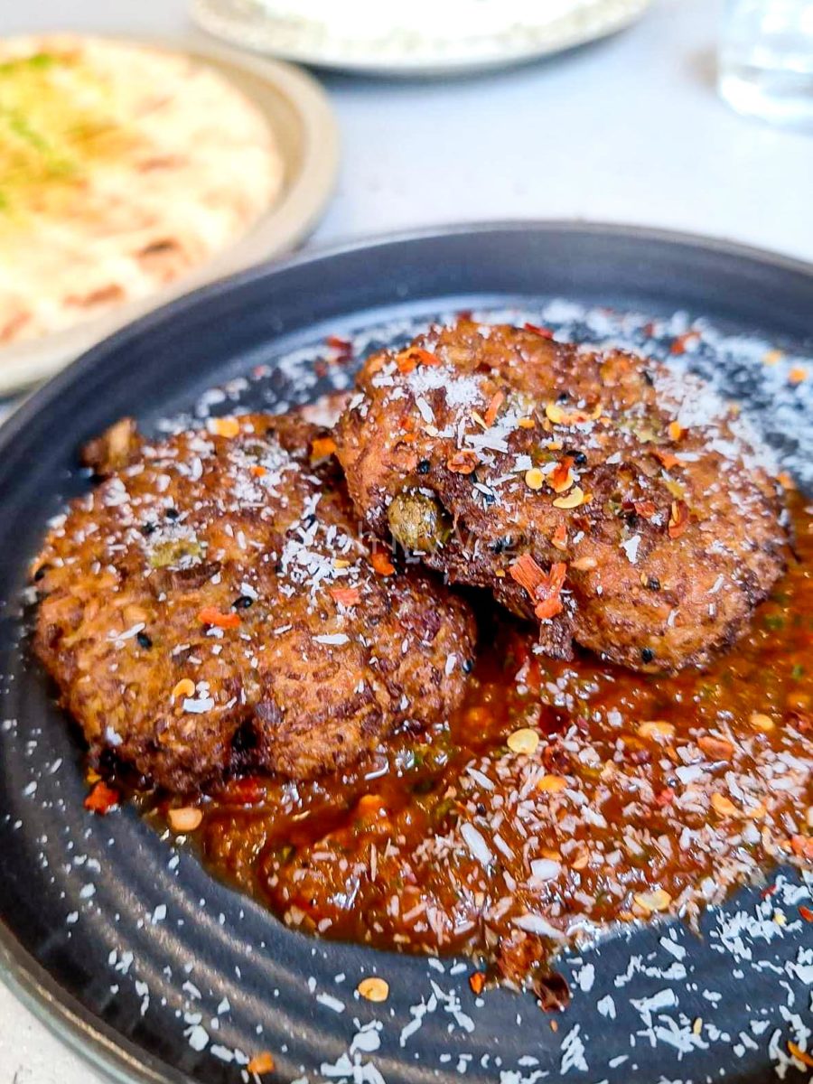 Maray Manchester cauliflower bhaji with red pepper dip, coconut, and chilli on a black plate. 