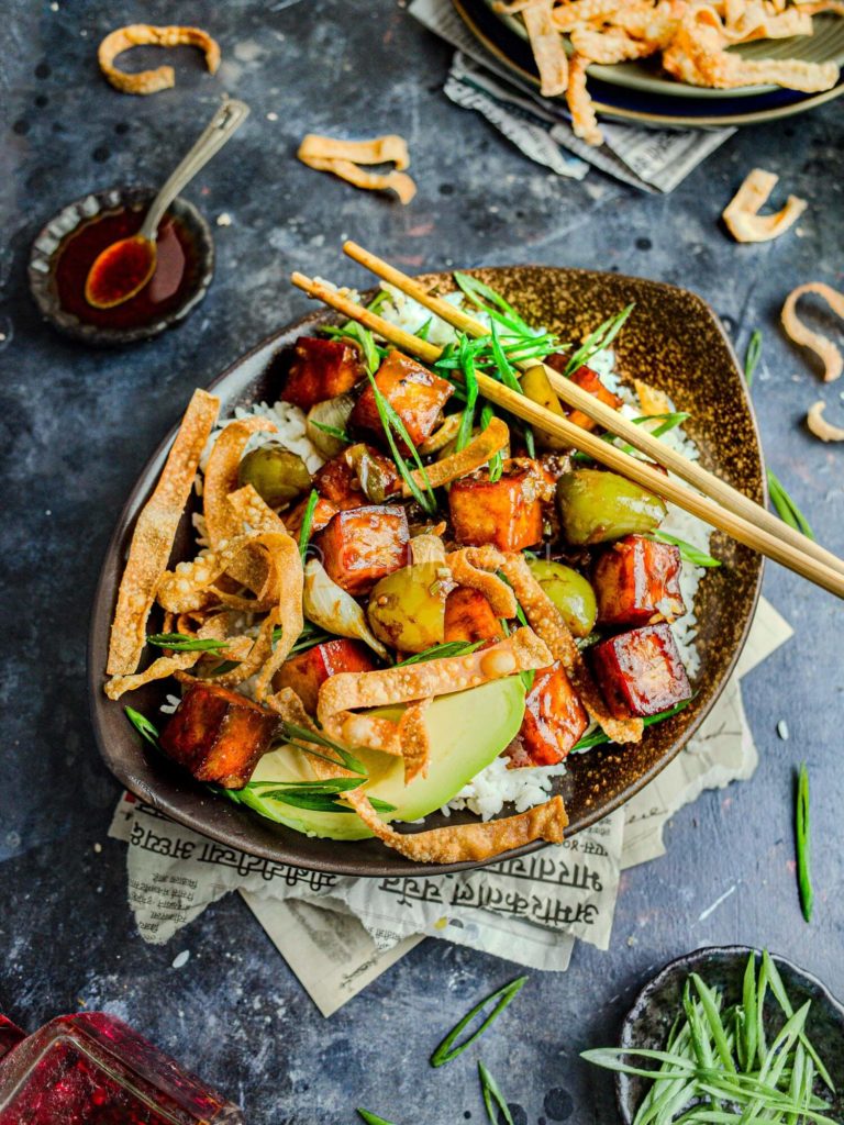Vegan Indo-Chinese chili paneer in a bowl with rice, avocado, and wonton crisps.