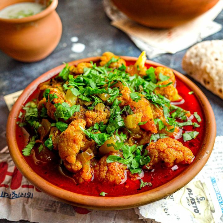 Maharashtrian Flower Batata Rassa in a clay pot, with raita and bhindi masala in the background.