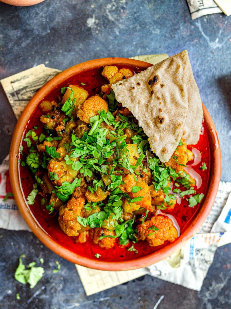 Maharashtrian Flower Batata Rassa topped with coriander in a clay bowl, with a torn off piece of chapati on the side. 