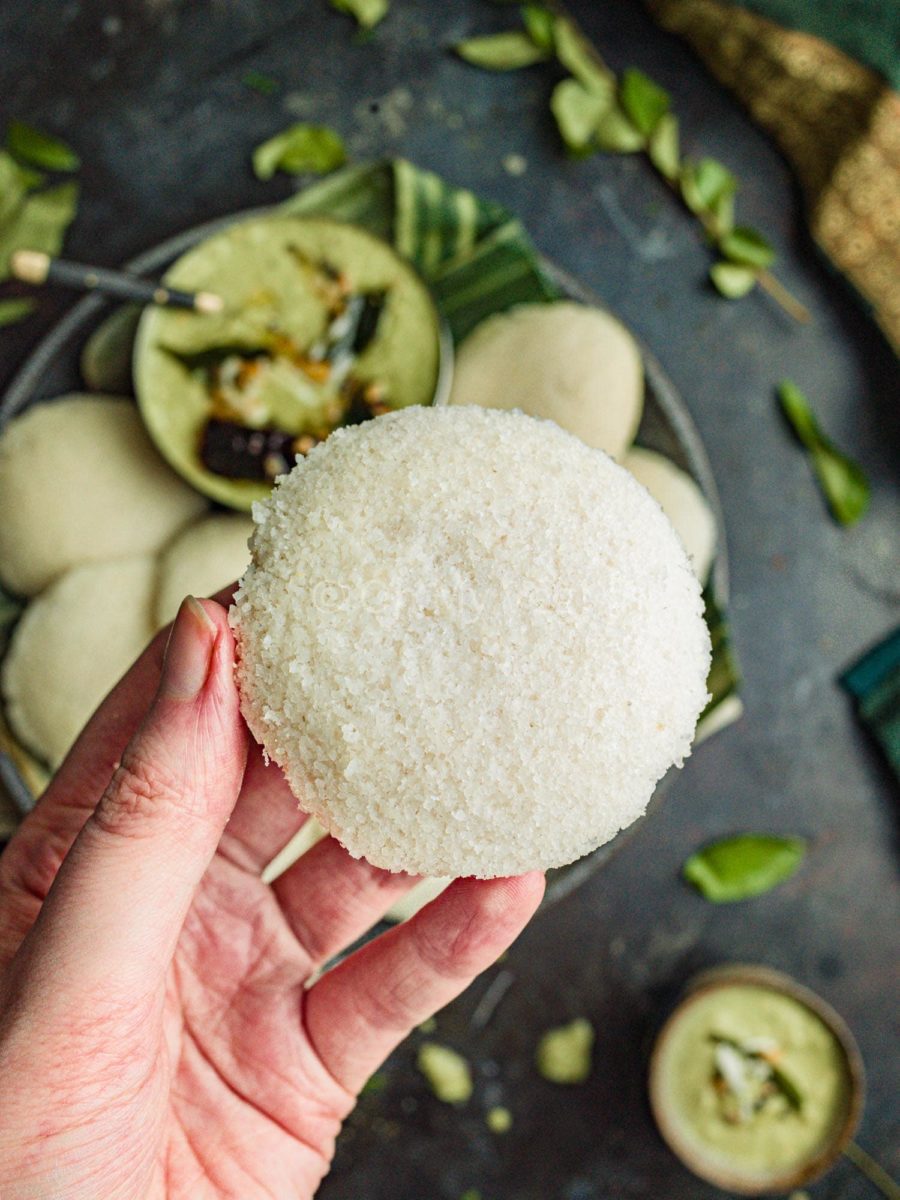 A woman holding a fluffy homemade idli. 