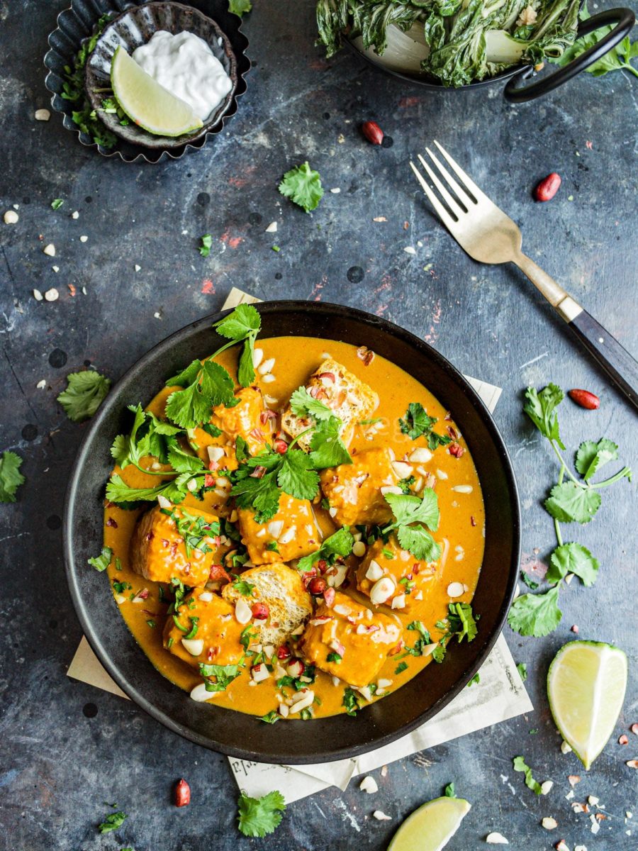 A bowl of tofu satay curry on a dark background.