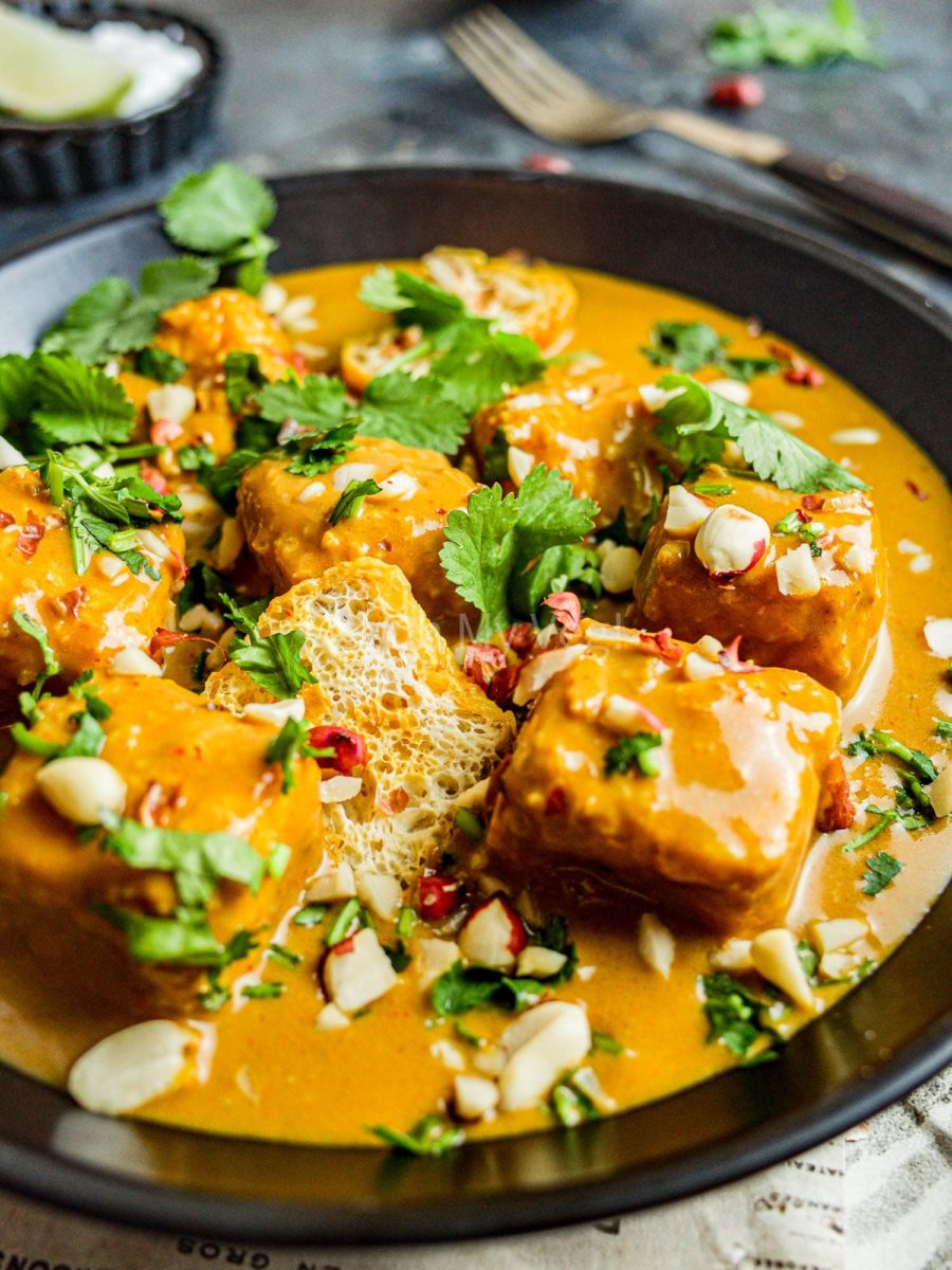Close up of tofu satay curry in a black bowl, topped with coriander and peanuts.