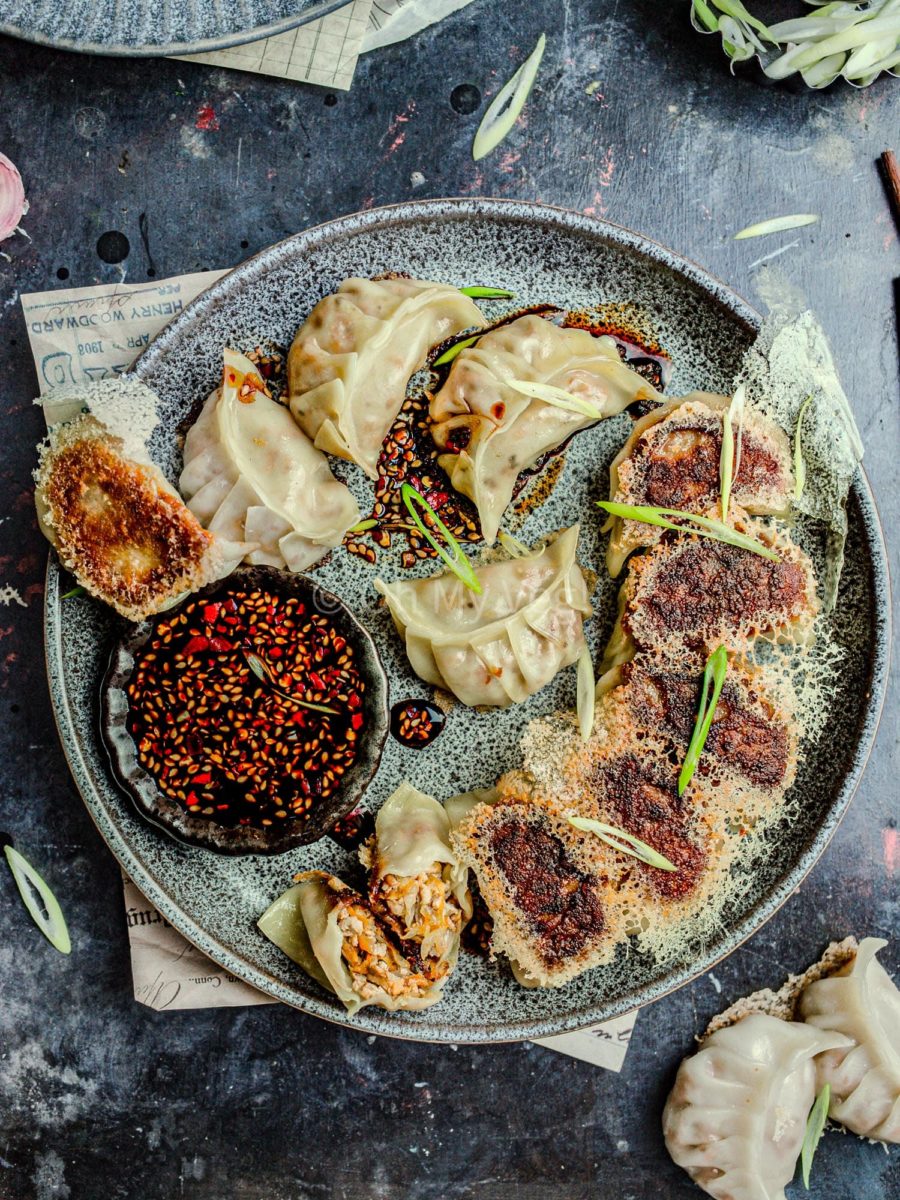 Vegan tofu potstickers with a crispy dumpling skirt on a grey plate, with dipping sauce.