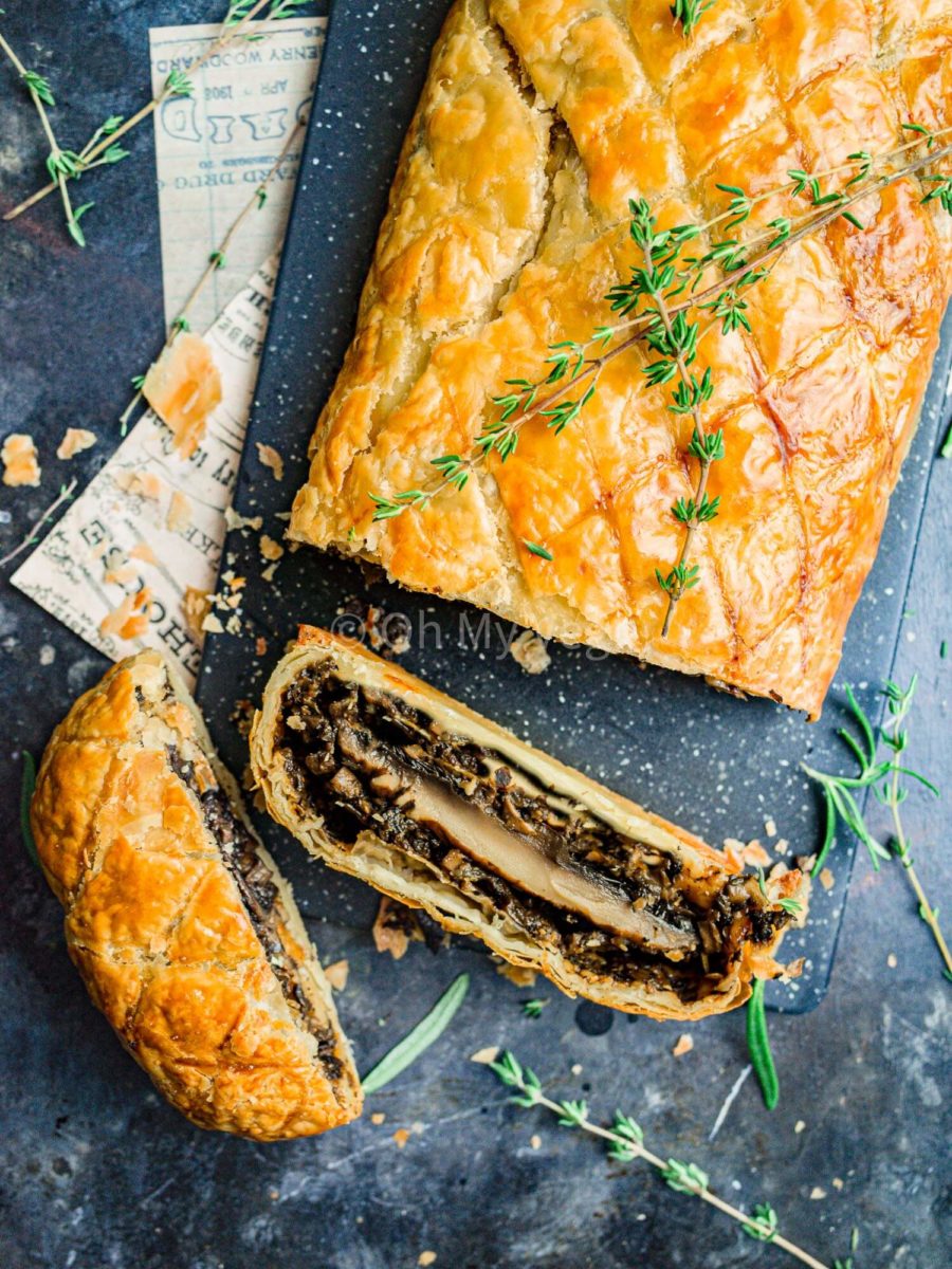 Two slices of mushroom wellington cut and laying on a dark blue board.