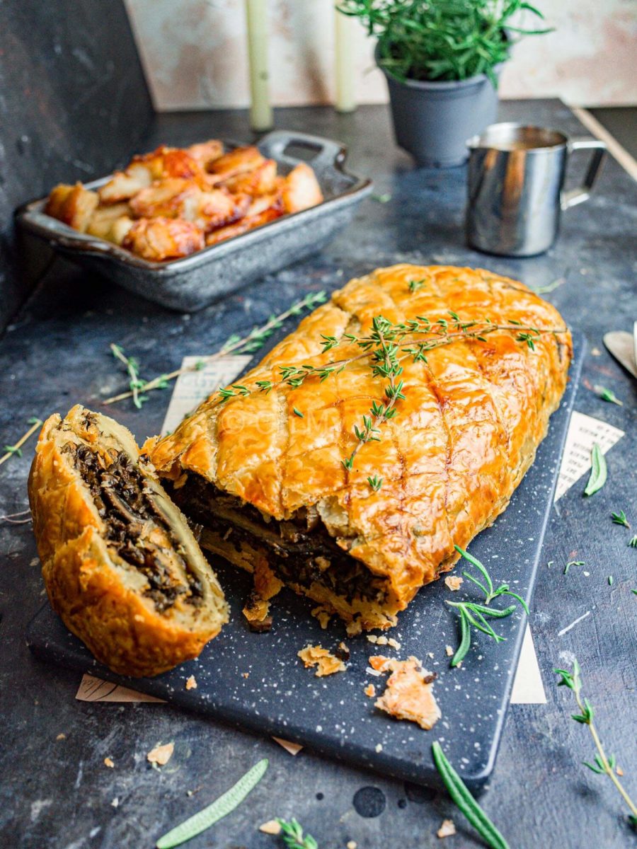 Mushroom wellington with roasted potatoes in the background, along with rosemary, candles, and gravy.