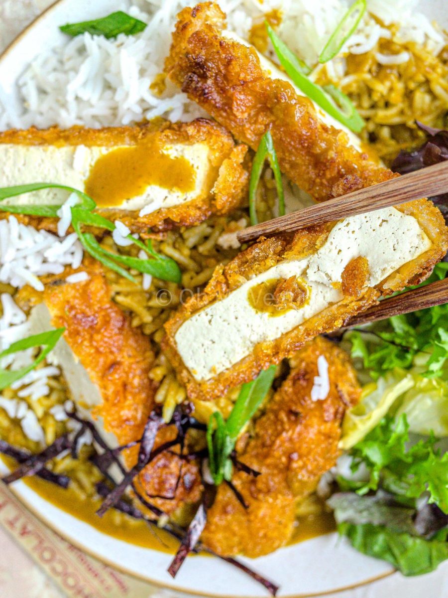 Chopsticks holding a piece of breaded tofu katsu.