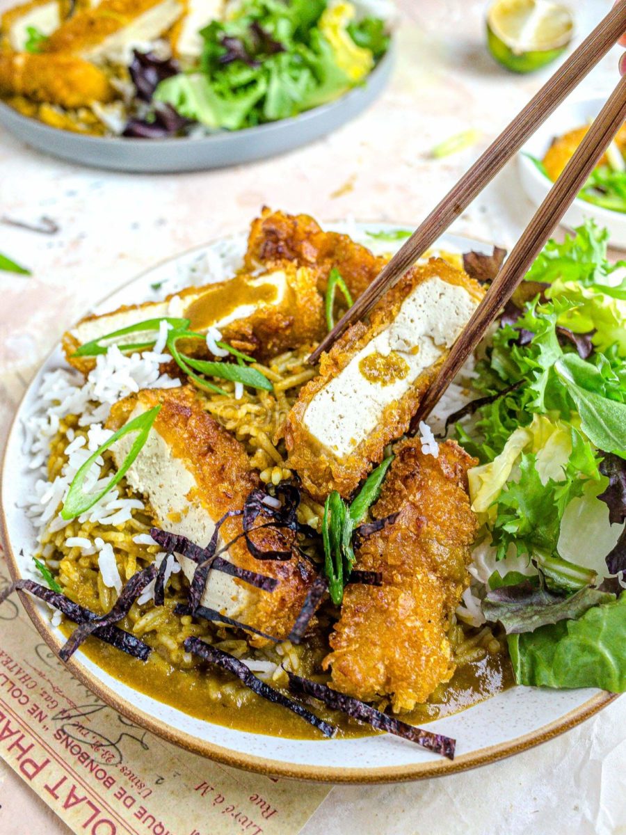 Tofu katsu curry on a plate, with chopsticks picking up a piece of tofu. 