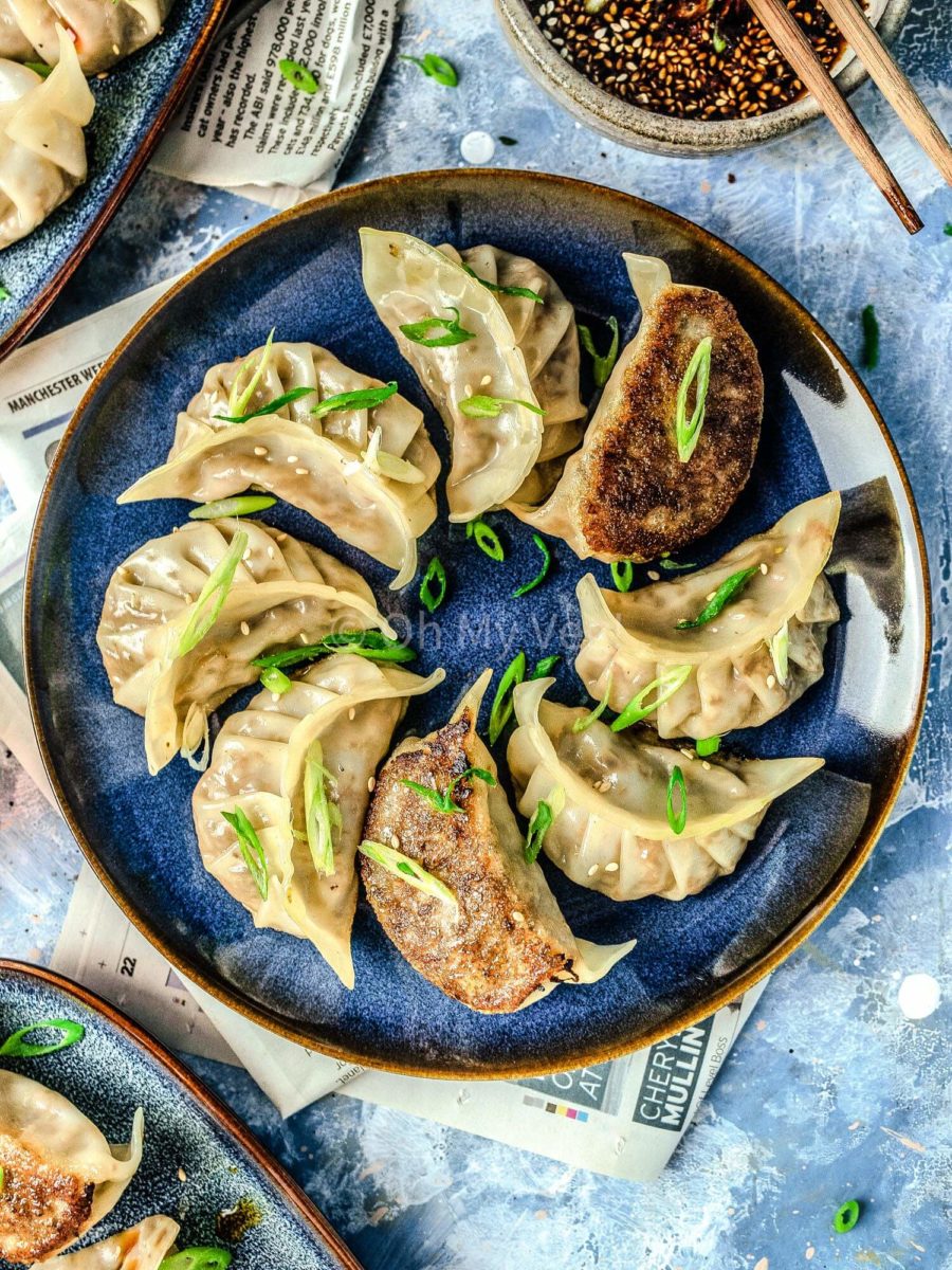 Vegan Japanese gyoza on a blue plate with spring onions on top.