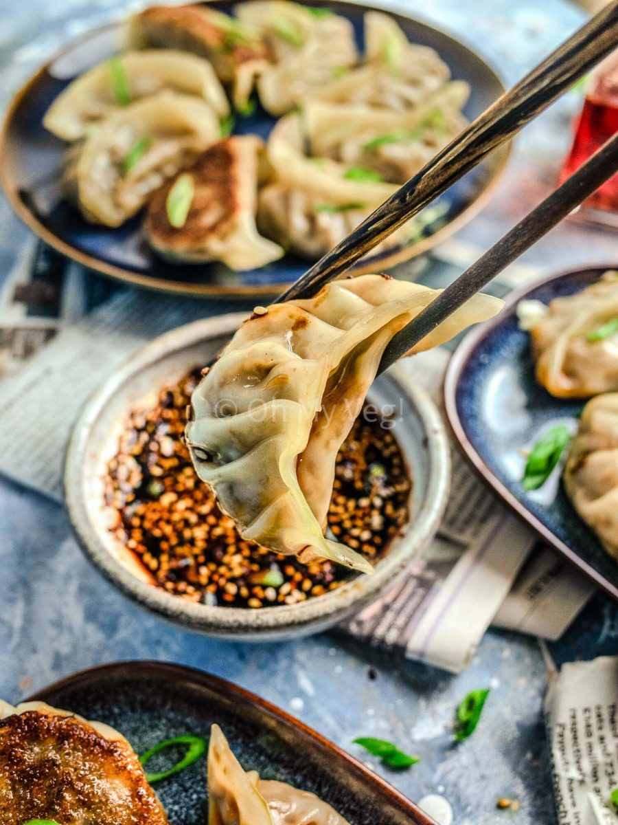 Chopstick holding vegan dumplings with dipping sauce in the back. 