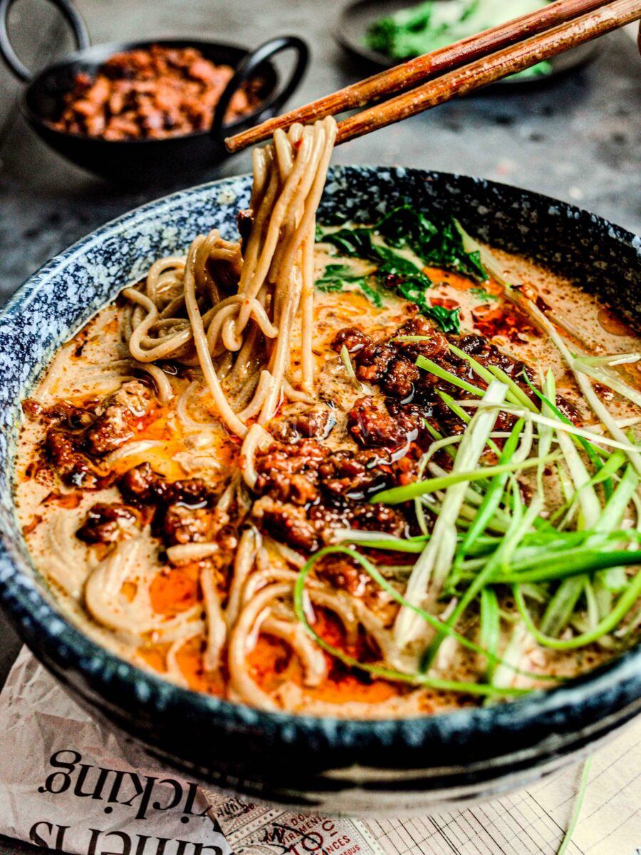 Chopsticks holding ramen noodles above a bowl of vegan tan tan men. 
