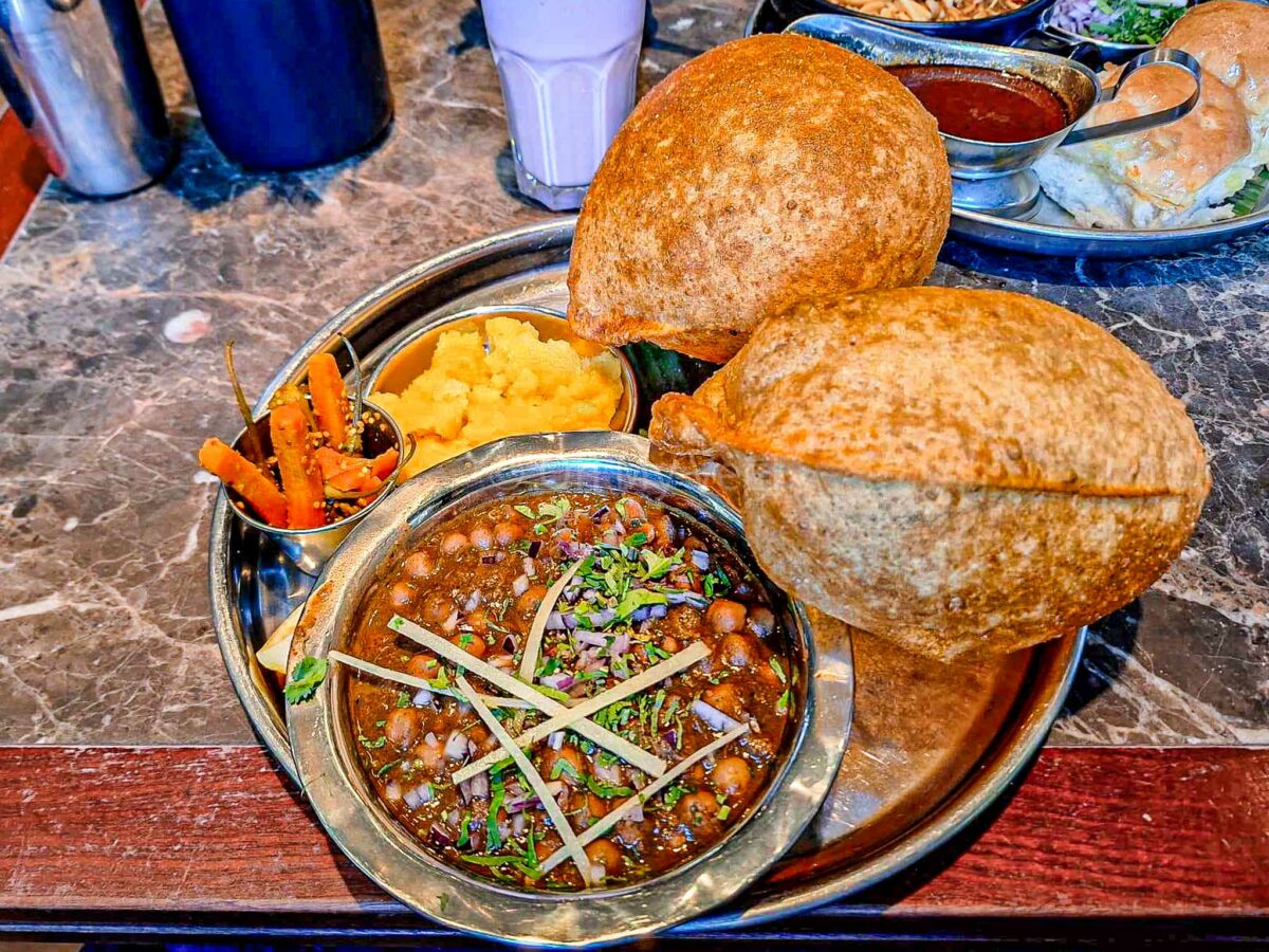 Chole puri with sooji halwa and pickles at Dishoom Manchester, on a marble table. 