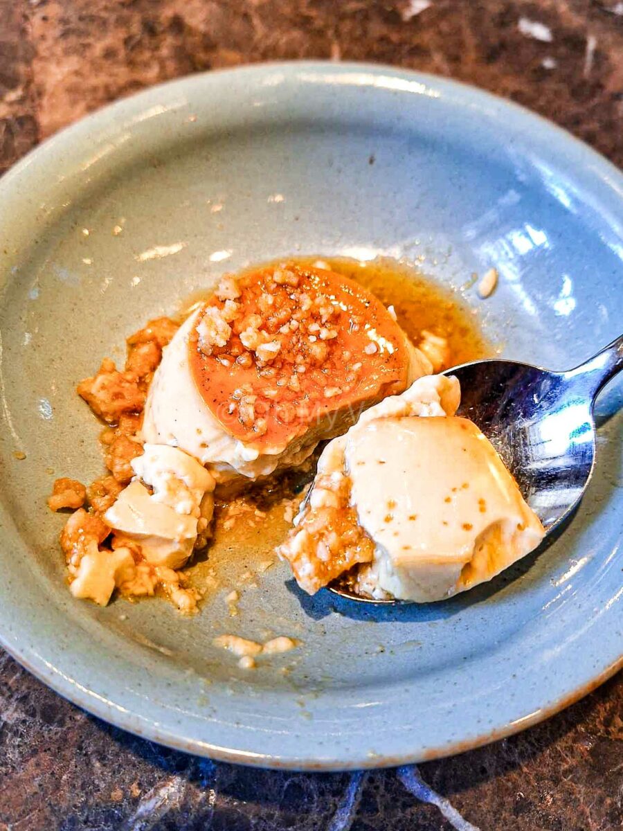 Coconut caramel custard with peanut chikki on a spoon.