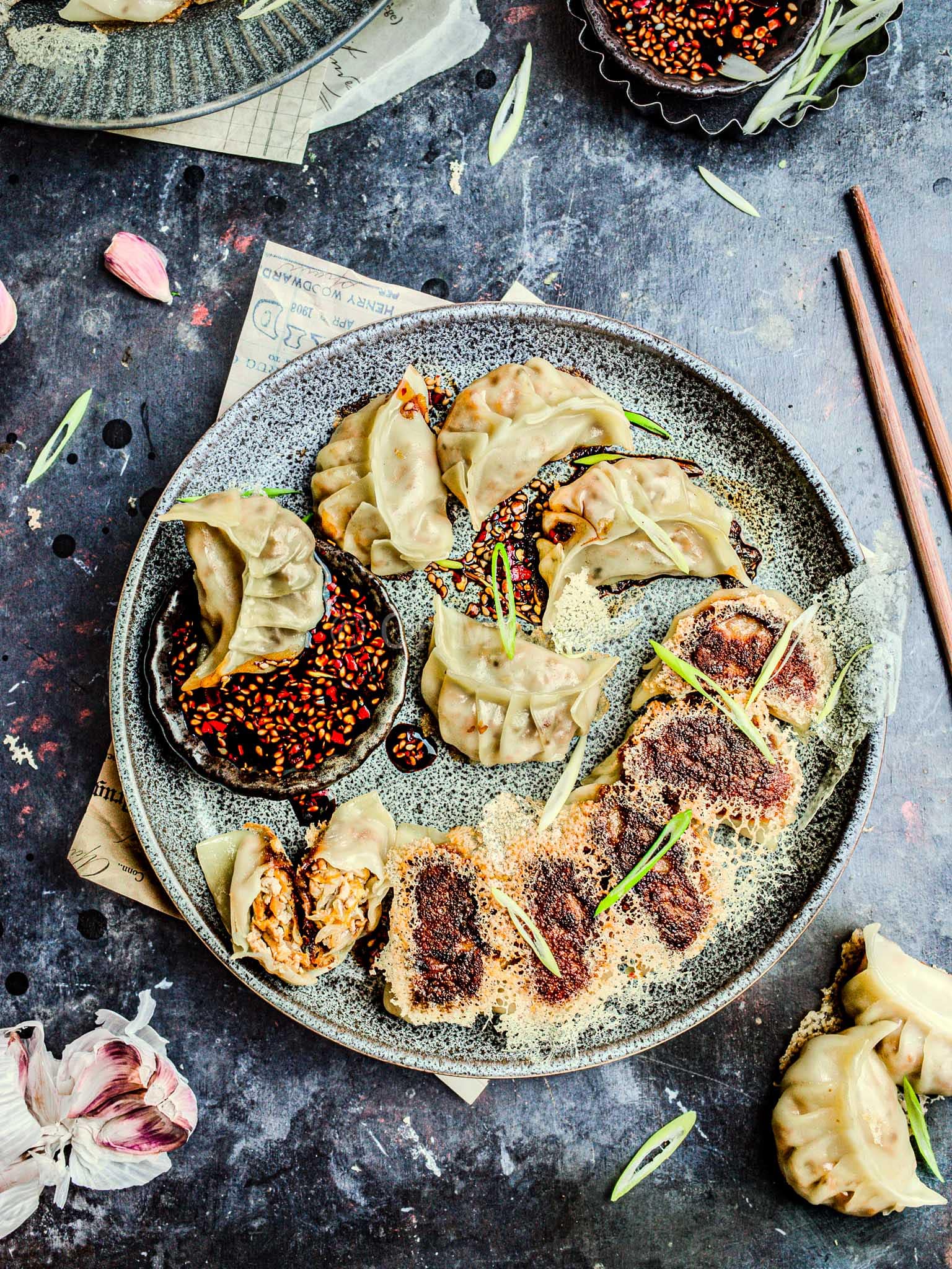 Vegan tofu potstickers with a crispy dumpling skirt on a grey plate with a dipping sauce and chopsticks.